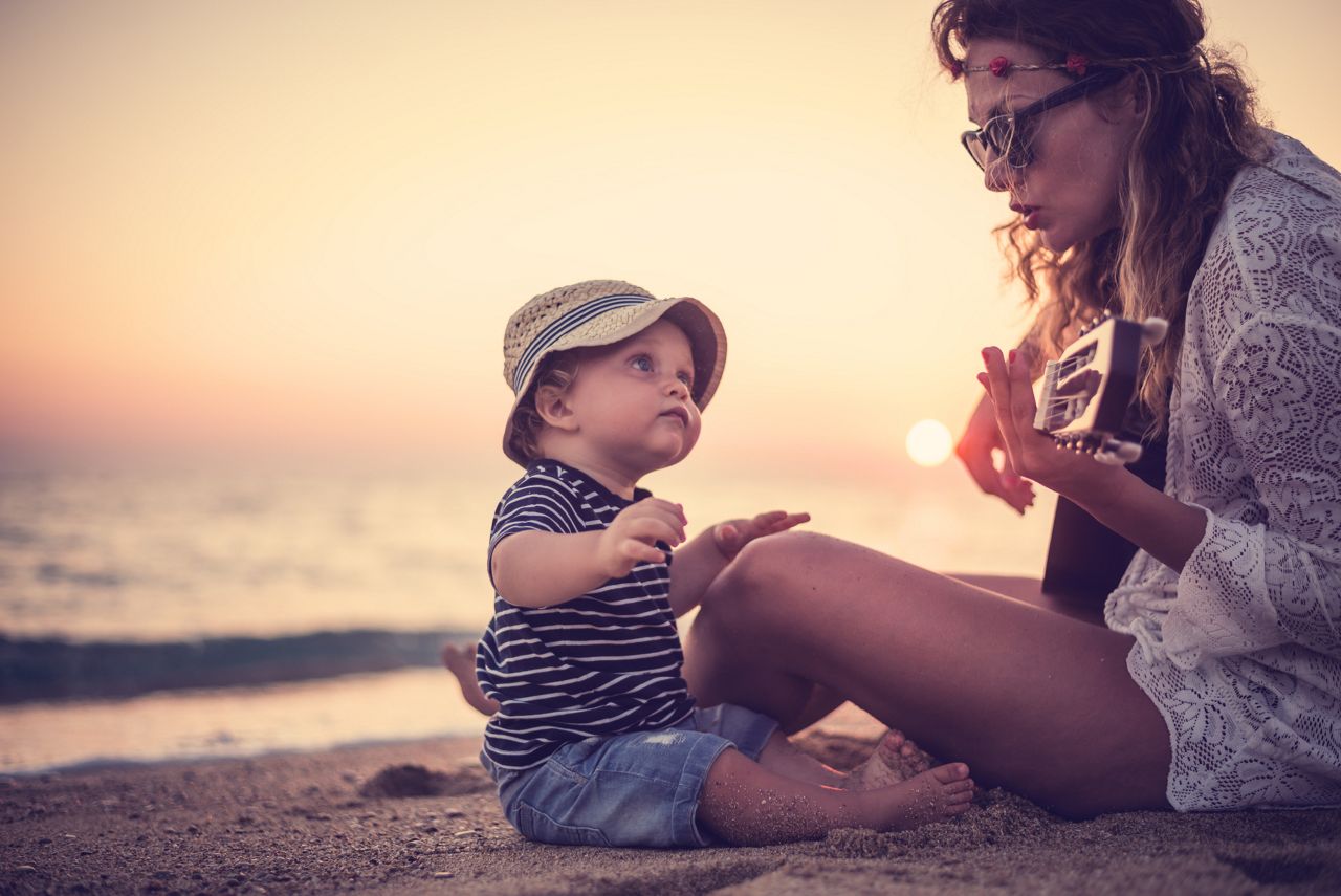 Mother playing a guitar for her son on the beach at sunset.