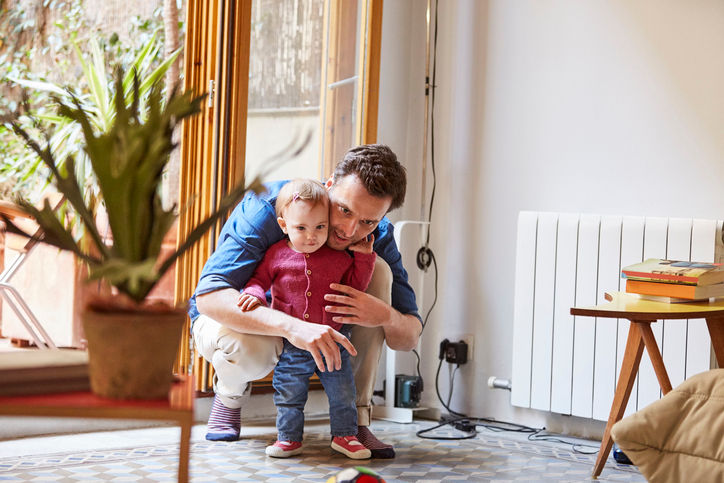 Mid adult man crouching while protecting baby. Father is with cute child at home. They are spending time together.