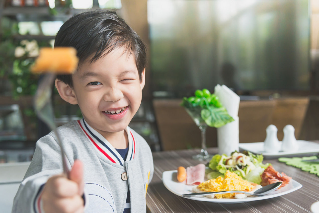 Cute Asian child eating breakfast in a restaurant