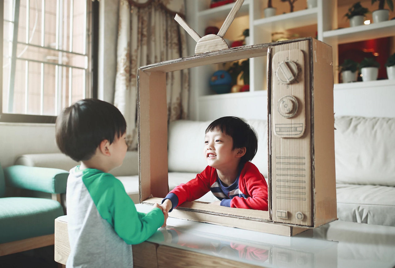 Boys play imagination game with cardboard tv
