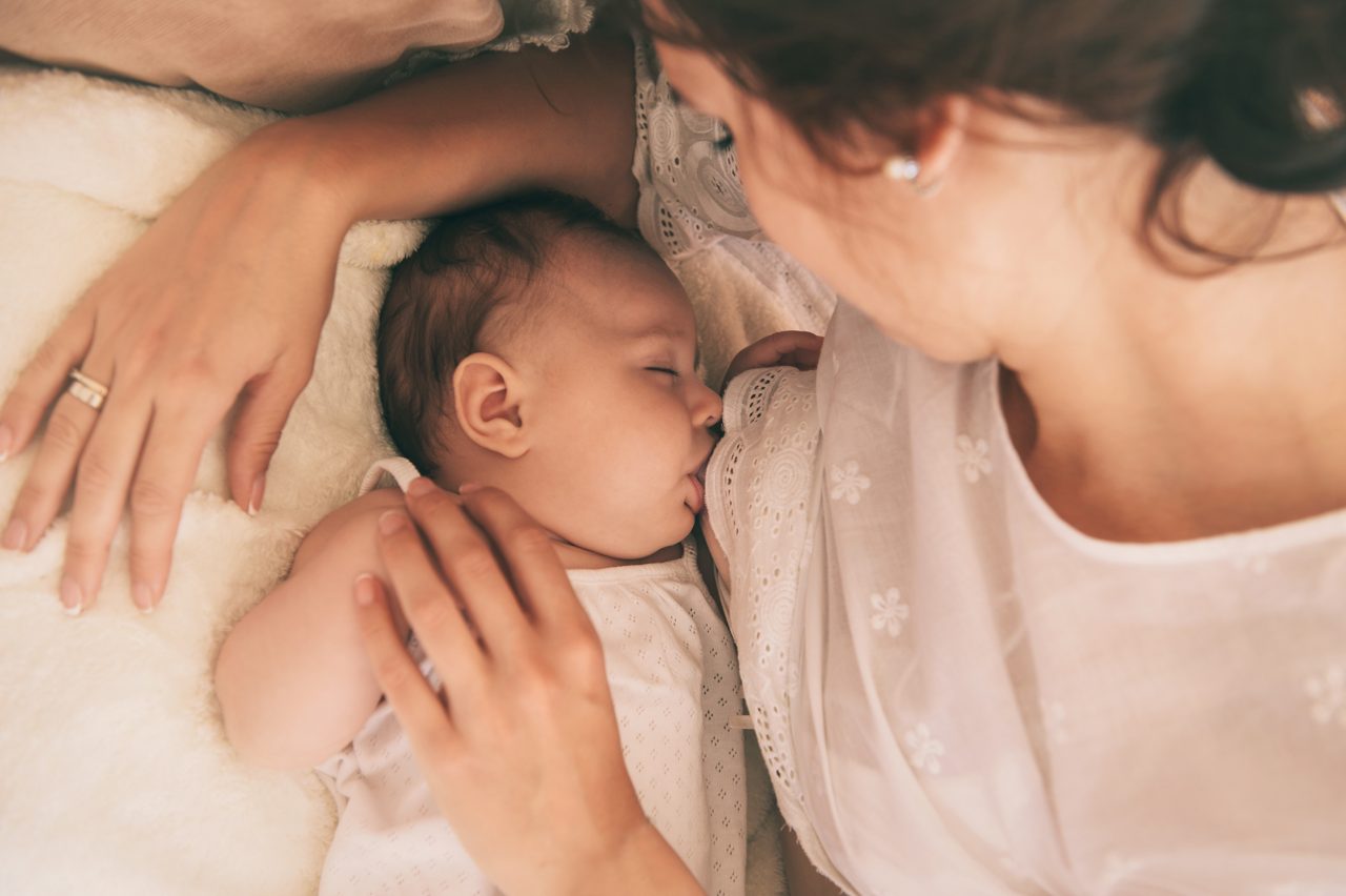 Beautiful young mom holding her 3 months baby. Mather nursing baby. Family at home.