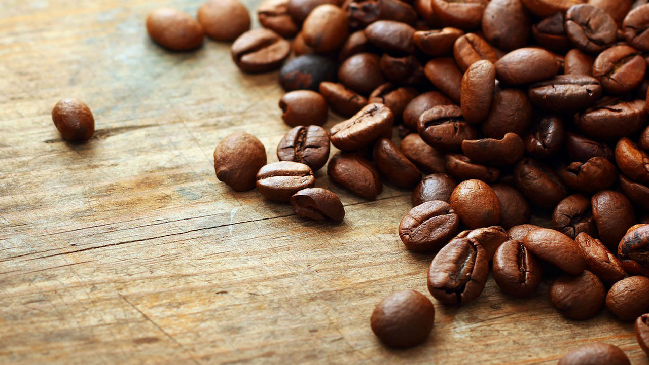 Granos de café sobre una mesa de madera, representando el consumo de cafeína y su impacto durante la lactancia materna