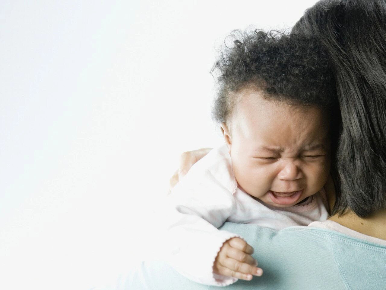 Mother hugging crying baby on bed