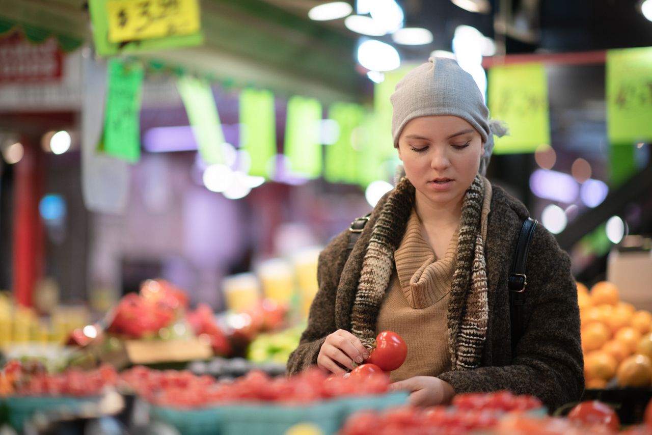 A beautiful woman with cancer is walking through a grocery store with a slight smile on her face.