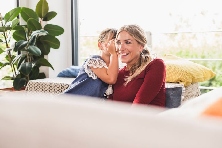 Girl whispering into mother's ear at home