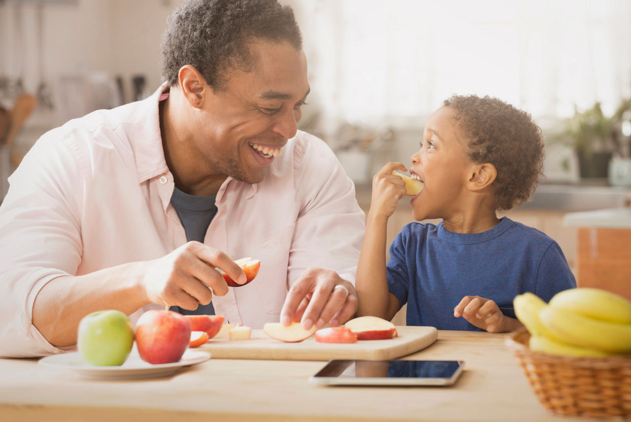 Mixed race father and son eating apples in kitchen