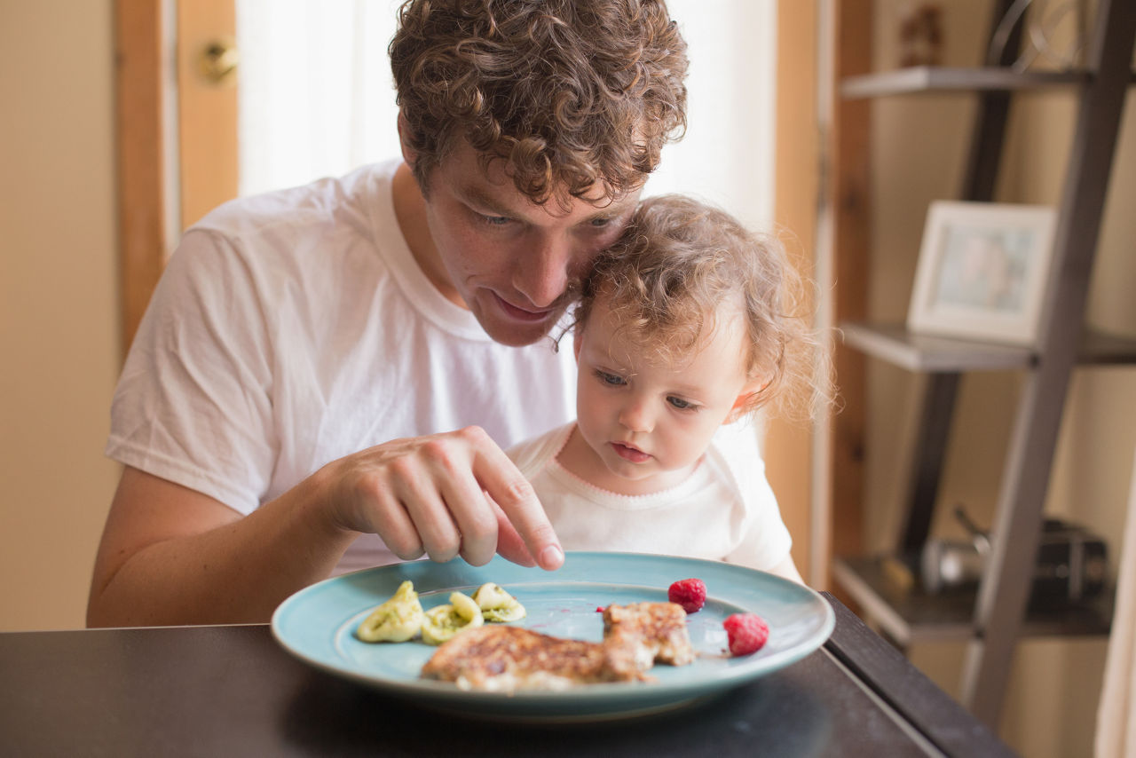 Father and his 1 year old daughter with meal at table in domestic home