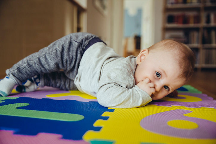 Baby boy laying on puzzle mat, putting fingers in mouth