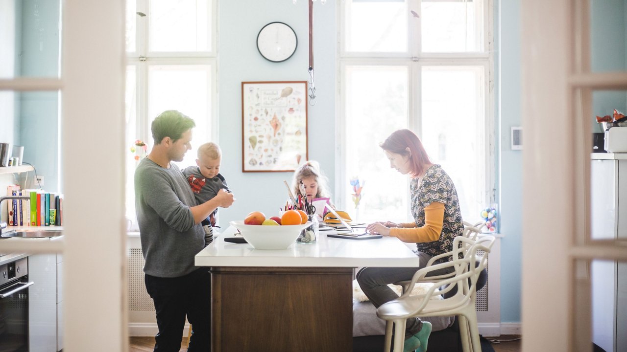 Familie sitzt am Esstisch, Mutter beim Laptop