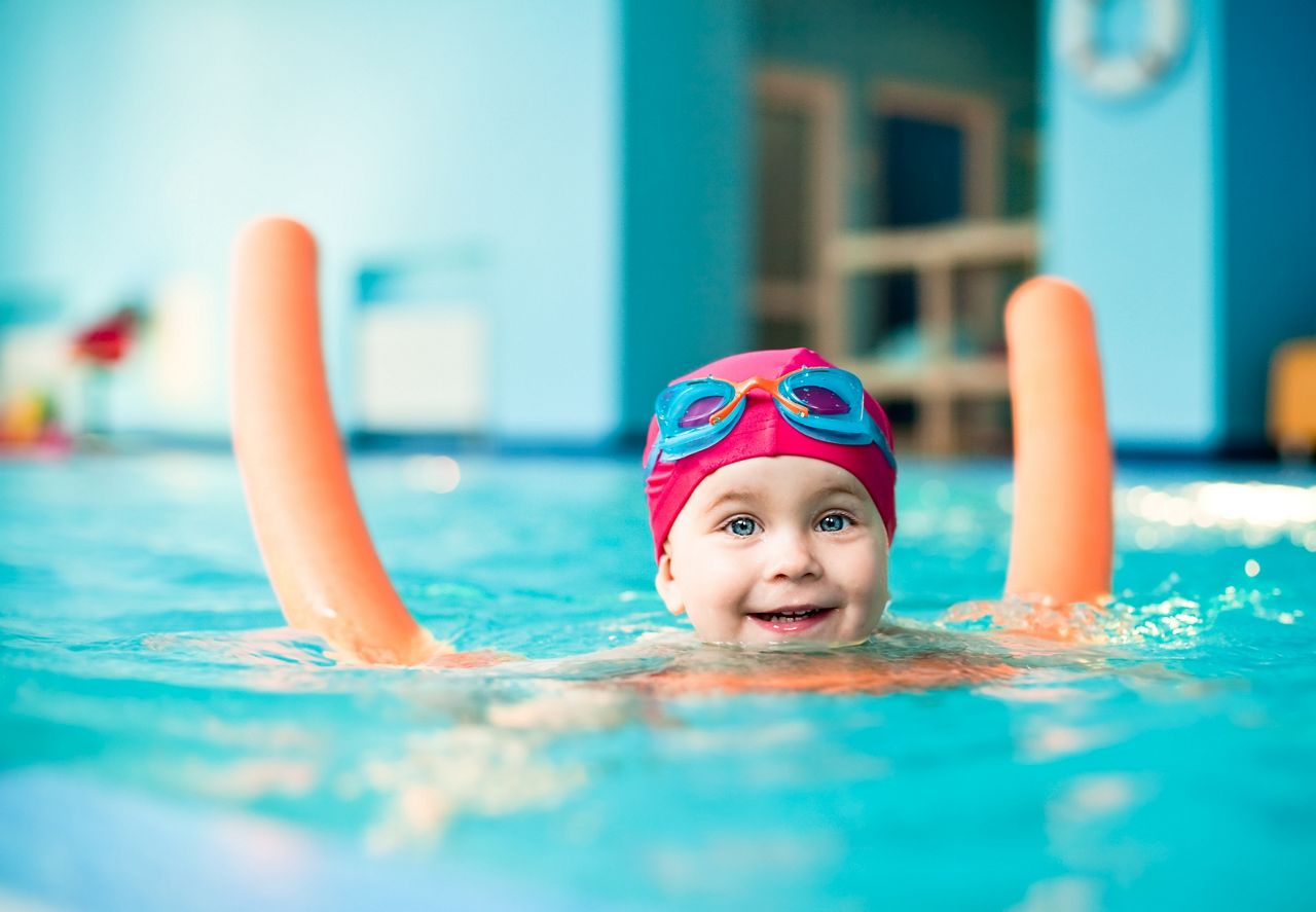 Happy little girl learning to swim with pool noodle