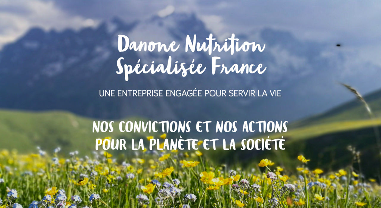 Une vue panoramique d'une prairie luxuriante avec des fleurs jaunes et bleues au premier plan, sur fond de montagnes majestueuses. L'image comporte un texte superpose affichant en evidence � Danone Nutrition Specialisee France � et un engagement envers les valeurs societales et environnementales. Le texte met l'accent sur les actions en faveur de la planete et de la societe.