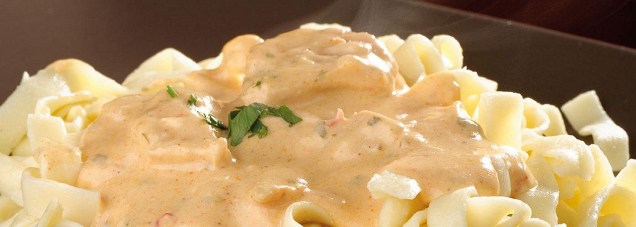 Bandnudeln mit cremiger heller Sauce und frischer Petersilie serviert auf einem dunklen Teller, Nahaufnahme des Gerichts.