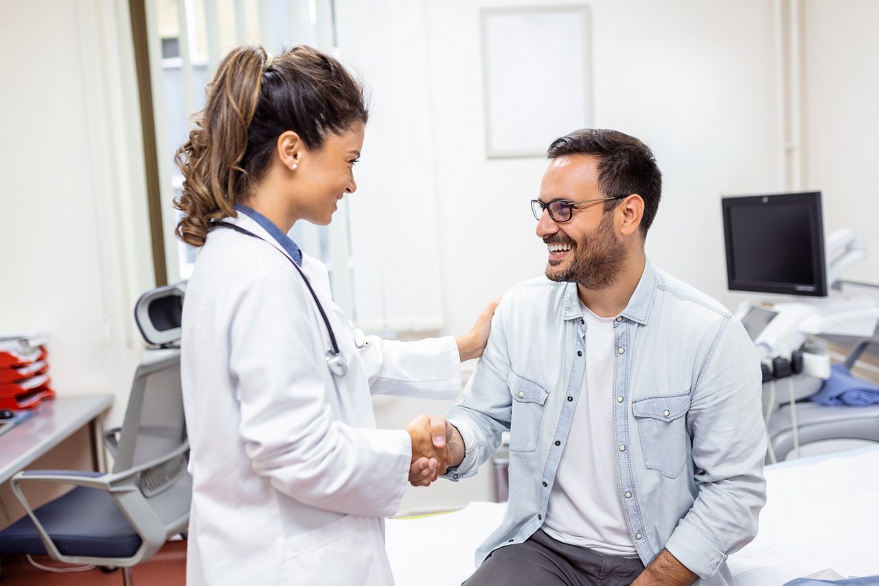 Smiling young female doctor shake hand close health insurance deal with elderly patient at consultation in hospital. Happy woman GP handshake greeting get acquainted with man in clinic.