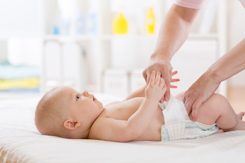 Mother putting diaper on her happy baby in nursery