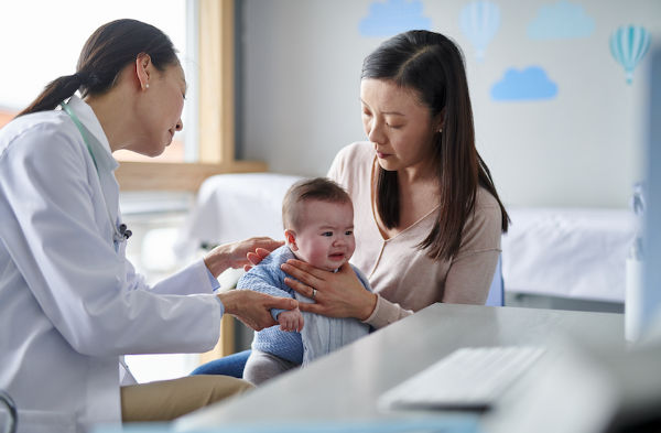 Mother holding baby while female medical professional does a check up