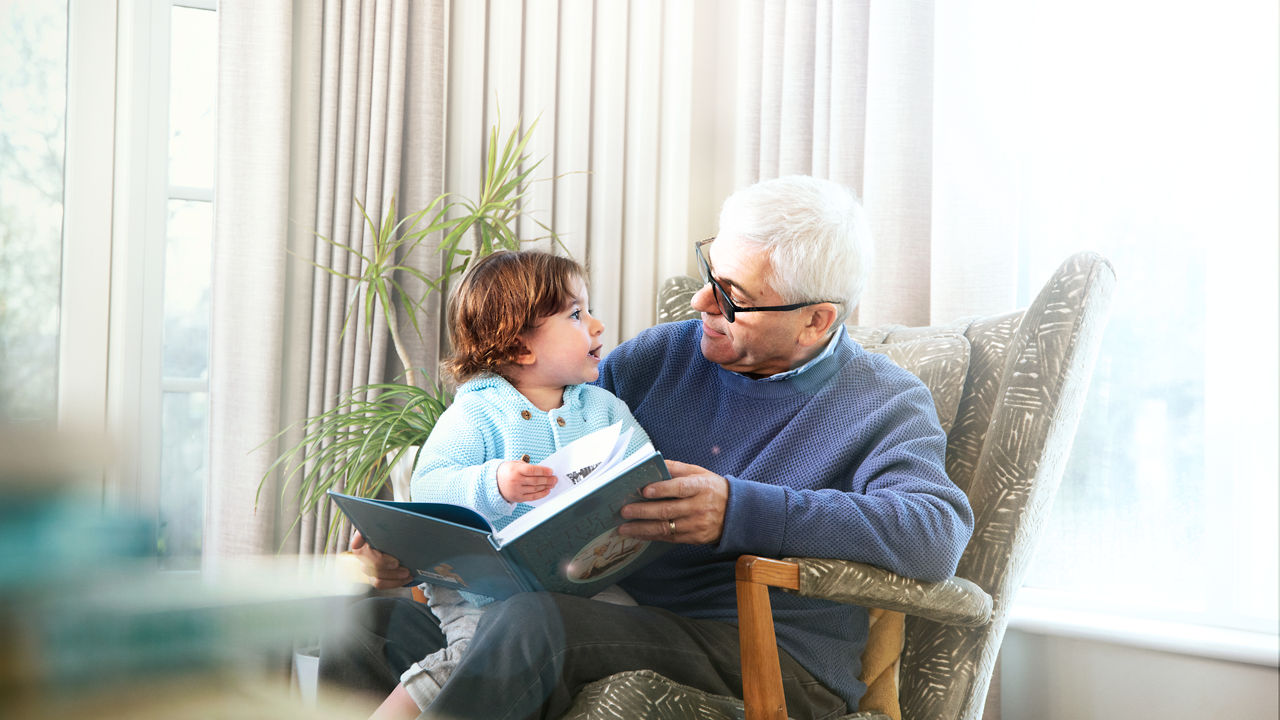 Grandad reading book to grandchild on his lap in armchair