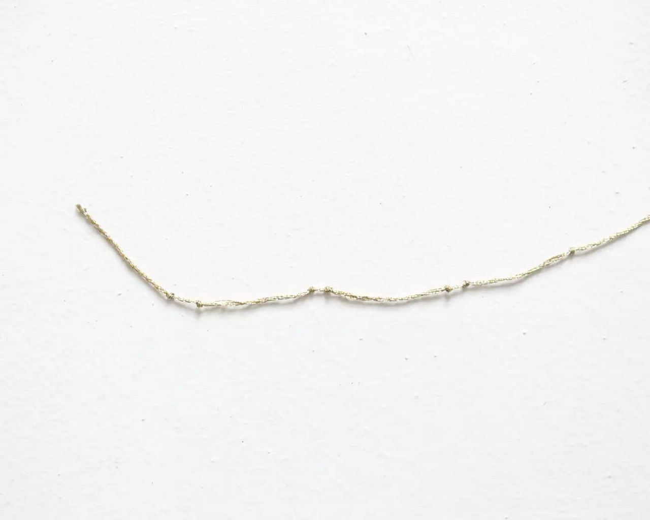 Un seul fil effiloche est presente sur un fond blanc immacule. Le fil semble delicat et texture, avec des fibres irregulieres visibles sur toute sa longueur. La composition minimaliste met l'accent sur la simplicite et les details, creant un visuel serein et discret.