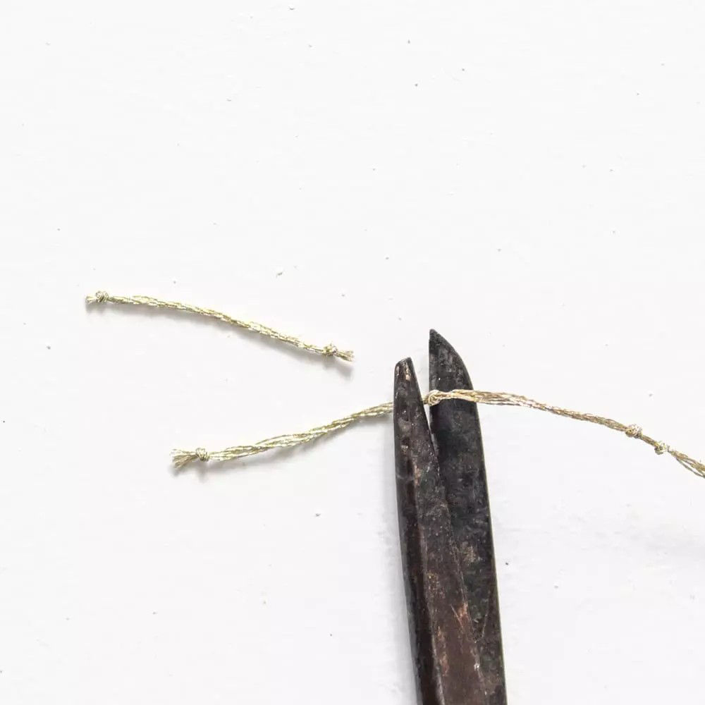 Une paire de ciseaux rustiques et vieillis est representee en train de couper un fil dore delicat sur un fond blanc uni. Les ciseaux ont une texture metallique patinee, ajoutant une touche vintage a l'image. Le fil dore est fin et effiloche aux extremites, soulignant une impression de fragilite et de precision.