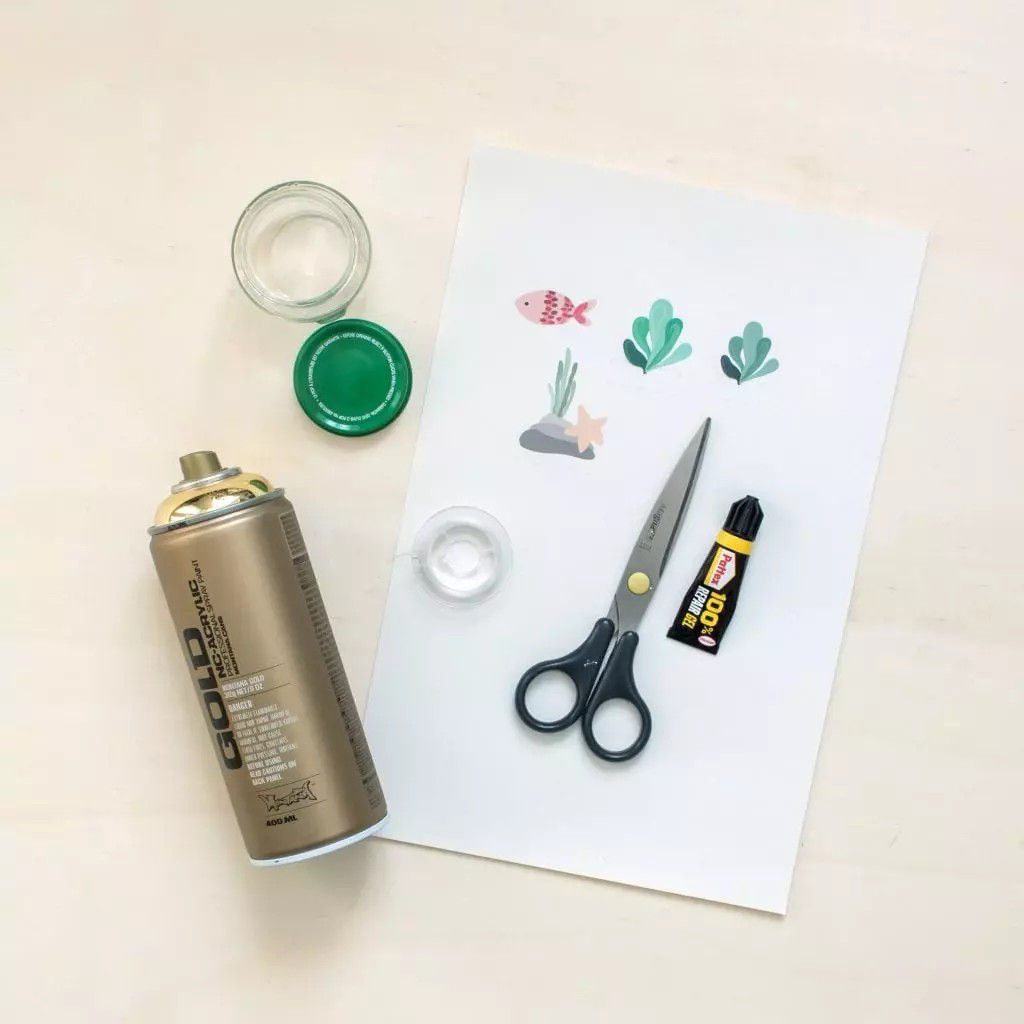 Une collection de fournitures de bricolage comprenant une bombe de peinture doree, des ciseaux, un tube de colle et des decoupes decoratives sur une feuille blanche. La bombe de peinture porte les inscriptions � GOLD � et � 400 ml �. Le tube de colle est noir et jaune avec l'inscription � UHU � visible. Le decor est un espace de travail epure et minimaliste avec une surface en bois clair.