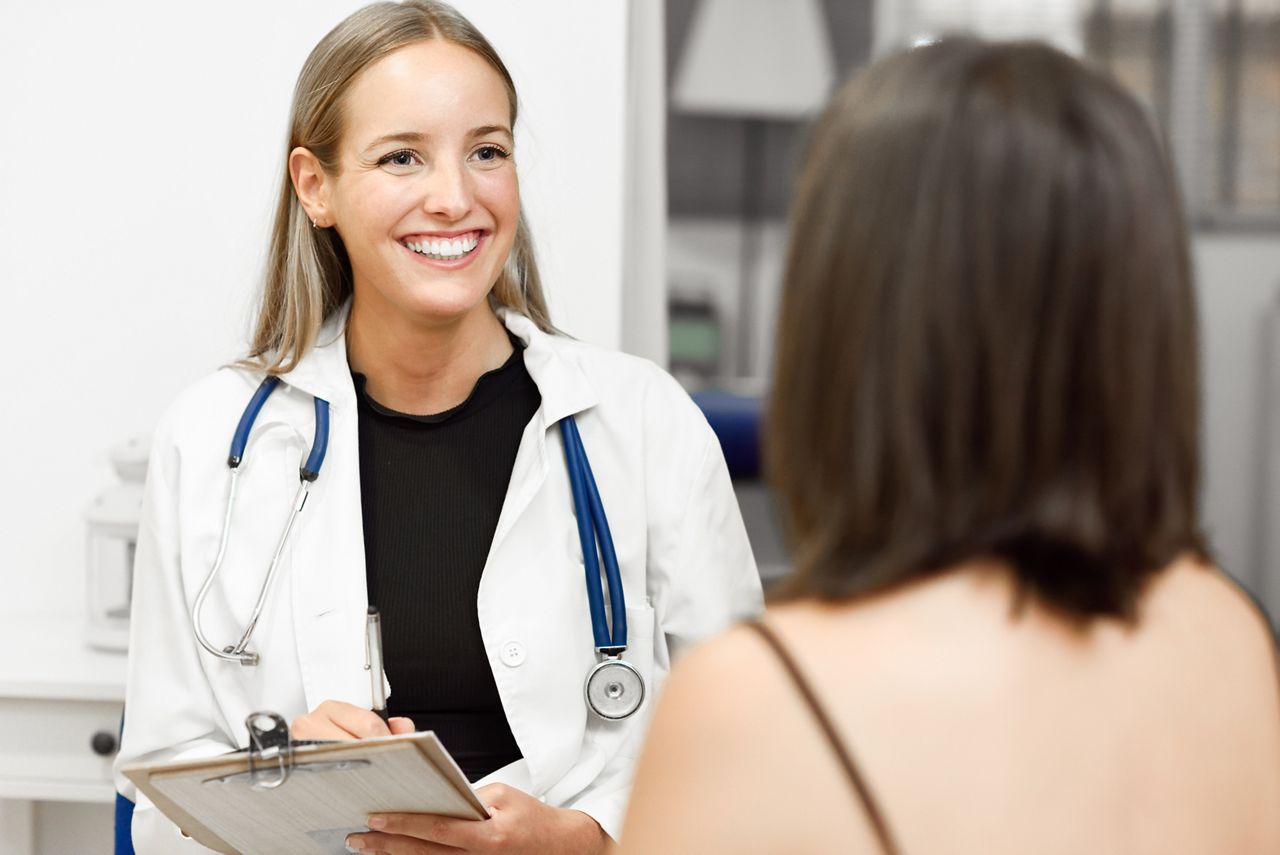 Female doctor explaining diagnosis to her patient. Brunette woman having consultation with smiling blonde girl in medical office.