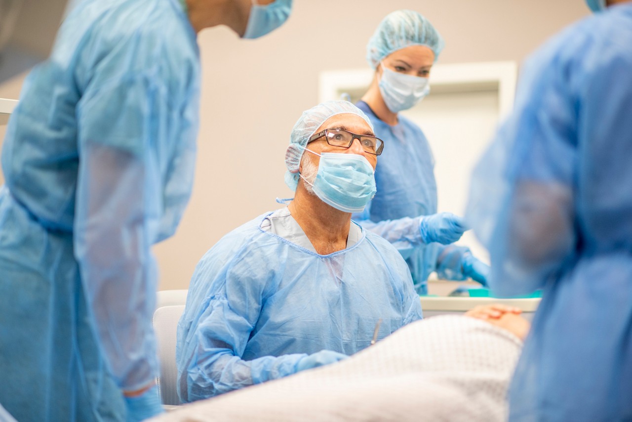 Male doctor in full medical infectious disease control attire sits next to pregnant patient as they prepare for cesarean birth.