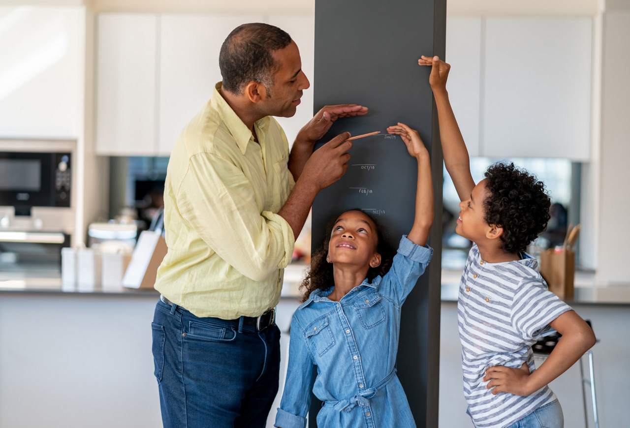 Faltering growth - father measuring their children next to a wall 