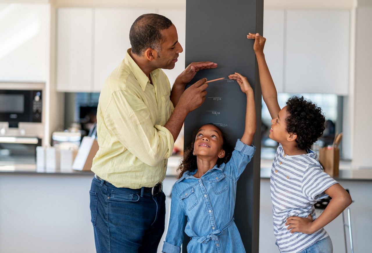 Faltering growth - father measuring their children next to a wall 