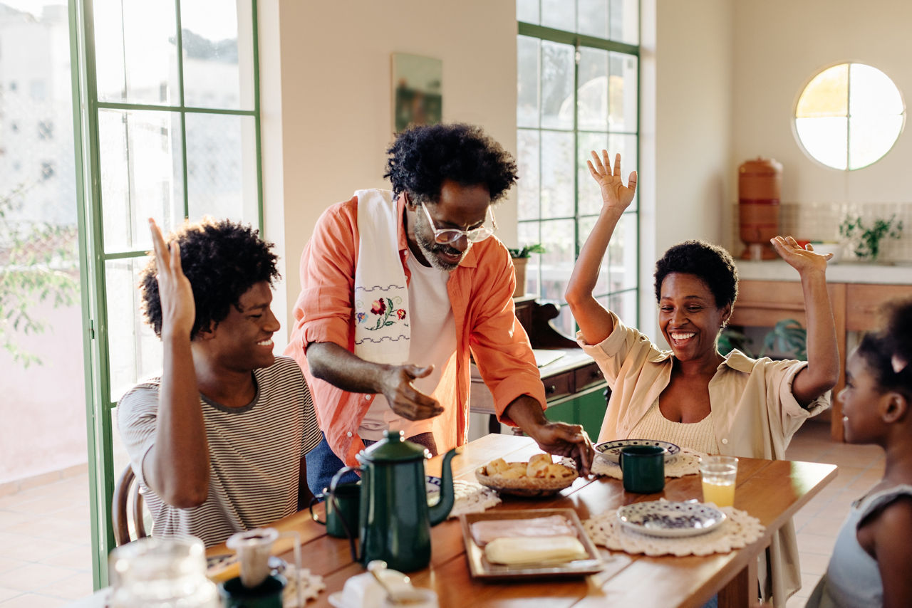 Black Brazilian family bonds over a delicious breakfast at home. Father serving pão de queijo, cheese bread rolls, to his excited wife and children. Family enjoying togetherness, happiness, and quality time in the kitchen.