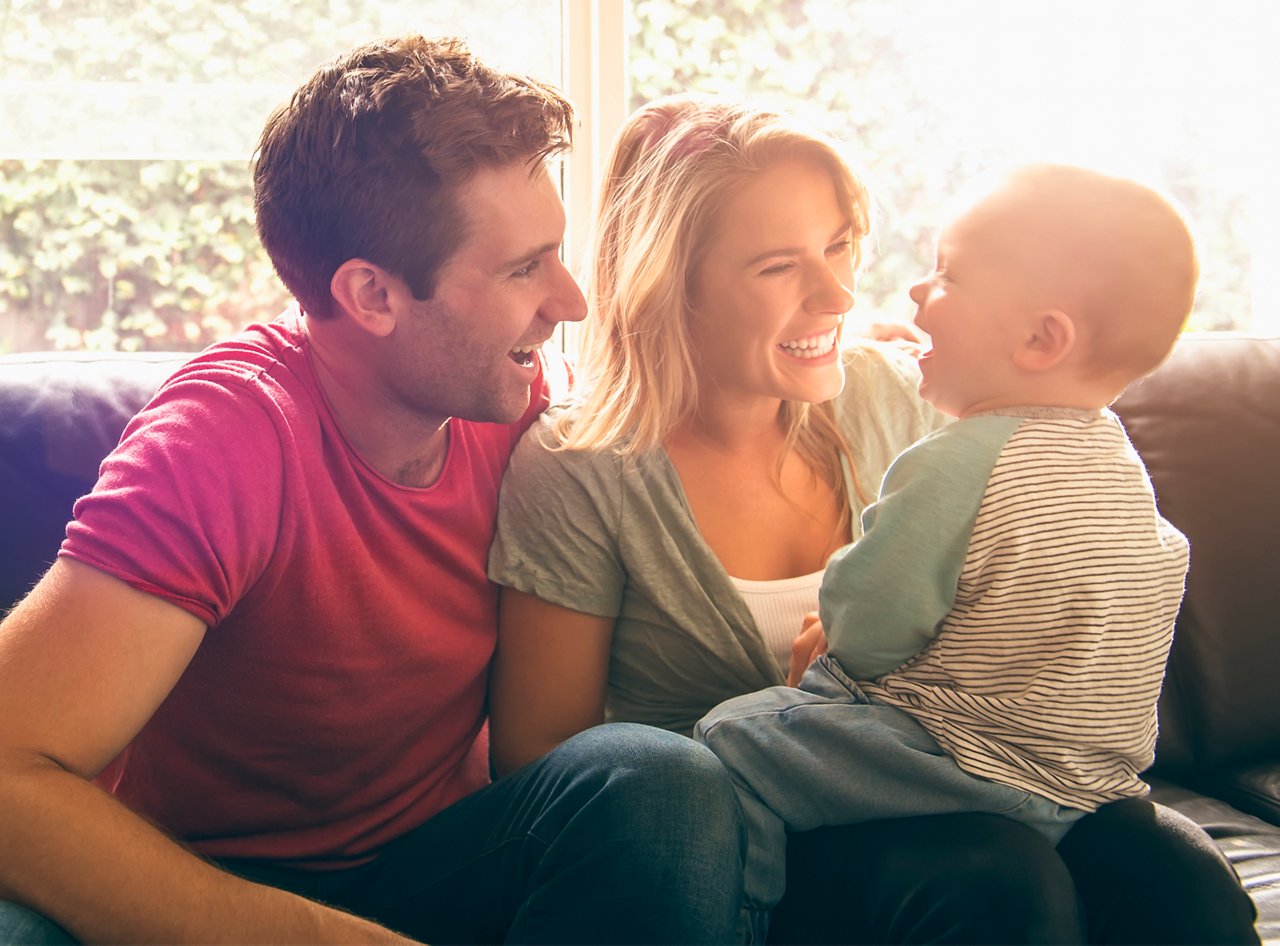 Eltern sitzen mit Baby auf der Couch und lachen