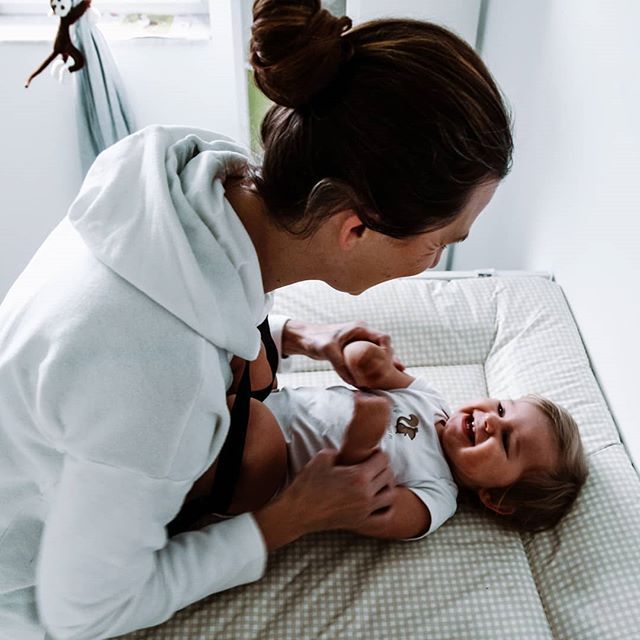 Mutter spielt mit lachendem Baby auf dem Wickeltisch