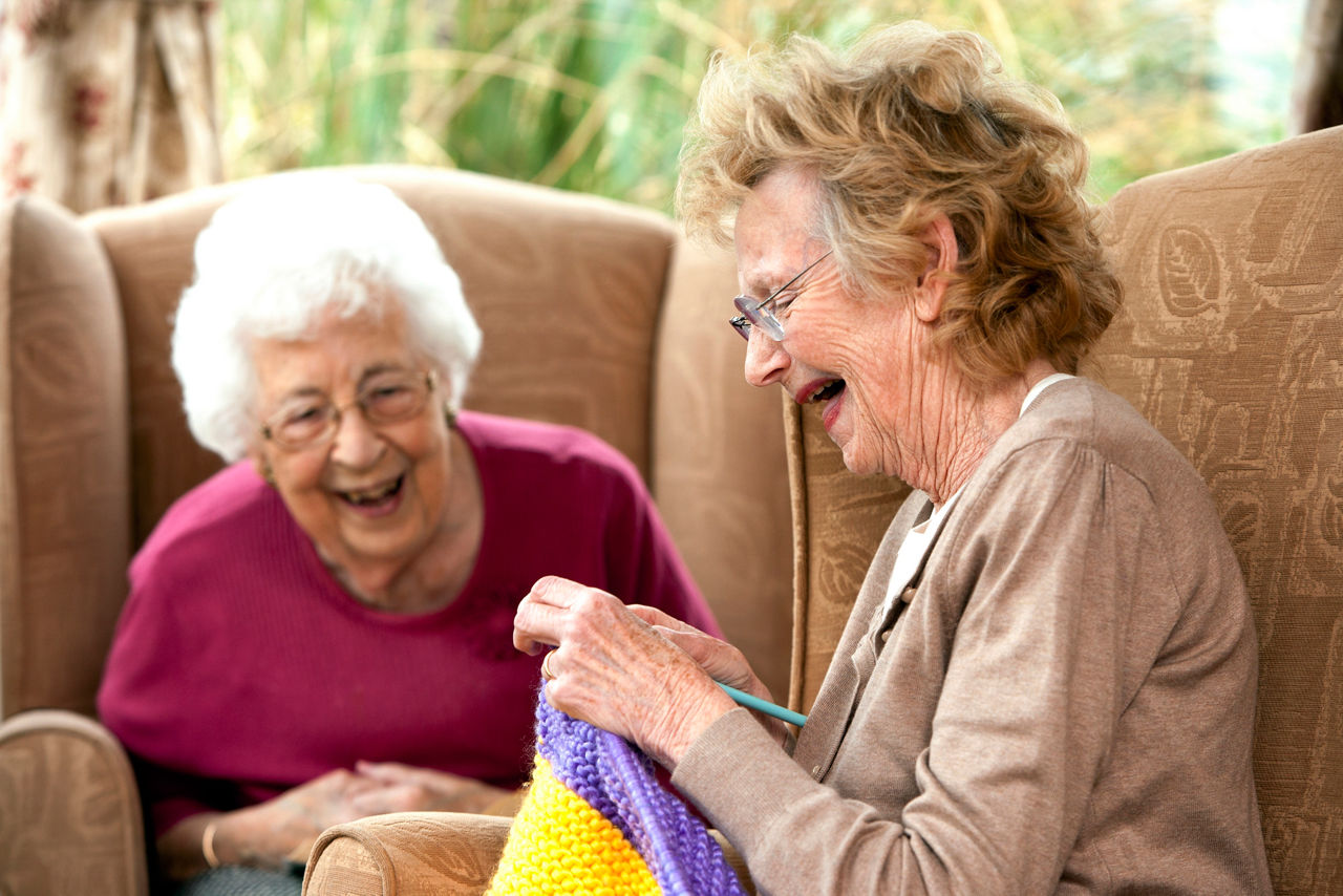 Elderly ladies laughing as one of them happily knits away.