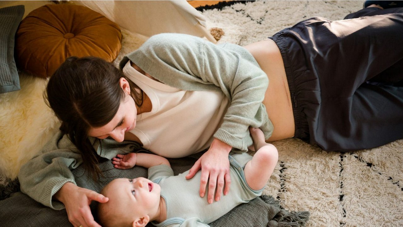 Baby und Mutter liegen lachend auf Boden auf Teppich