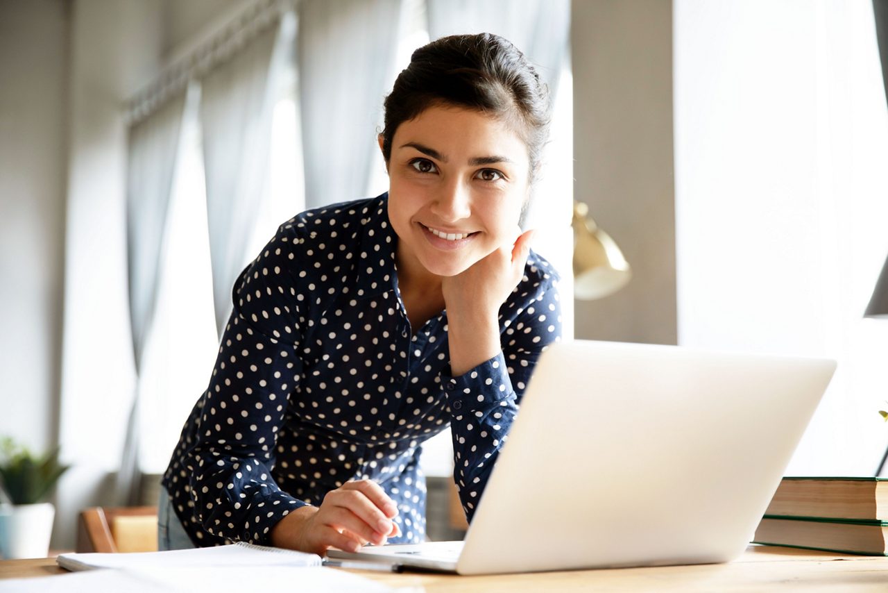 Portrait of smiling Indian girl stand at desk in living room working browsing Internet on modern laptop, profile picture of happy ethnic young woman busy surfing web, messaging typing on the gadget getty images 1208855983