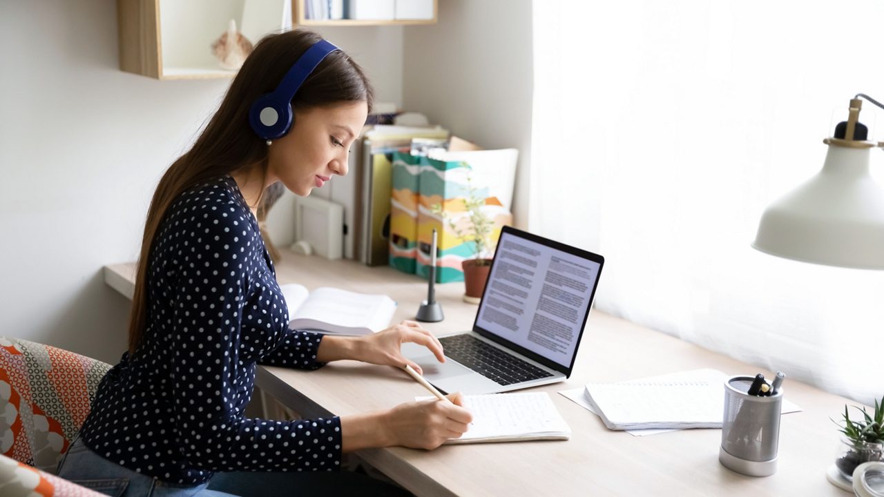 Side view focused young beautiful caucasian woman wearing wireless headphones, studying remotely using laptop at home office, smart millennial female student involved in research article writing.getty images 1279977817