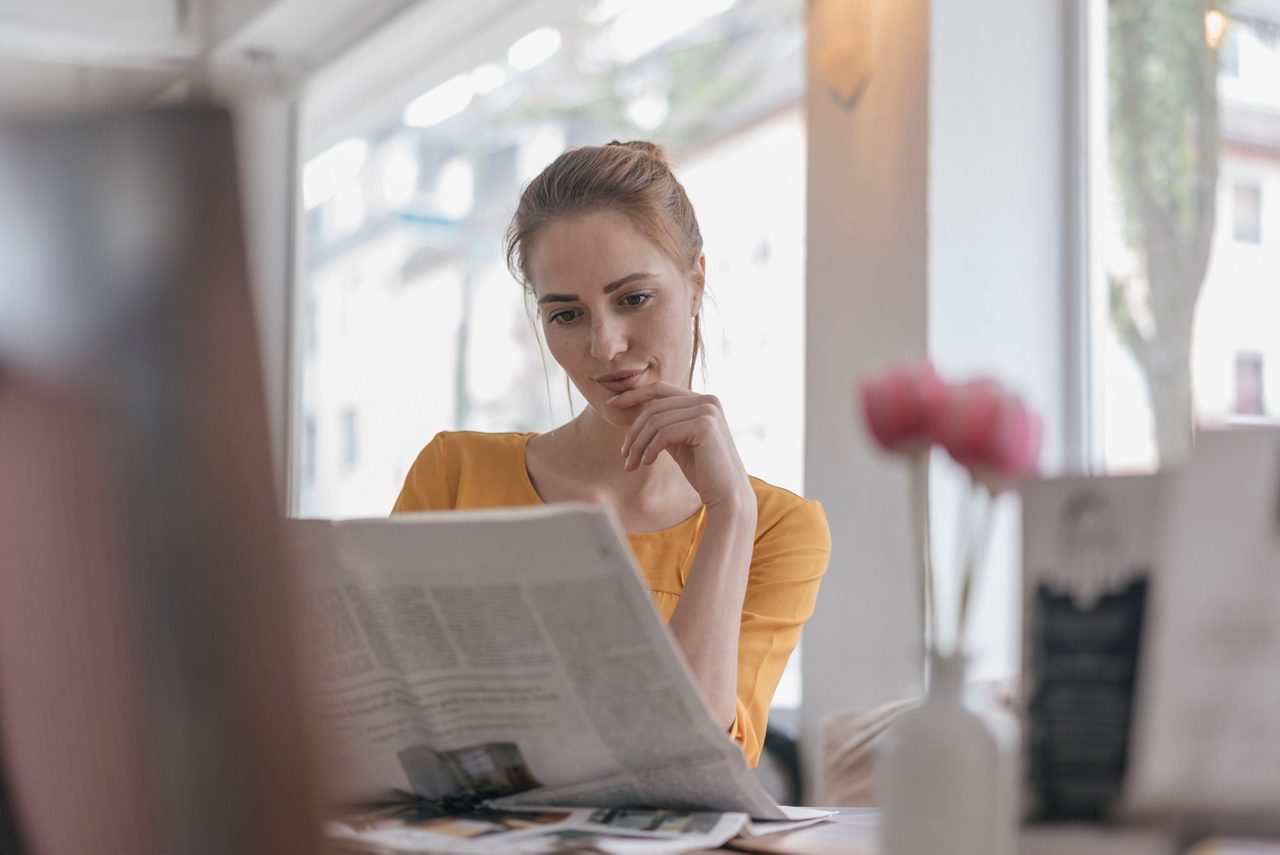 Young woman sitting in coworking space, reading newspaper getty images 1042692624