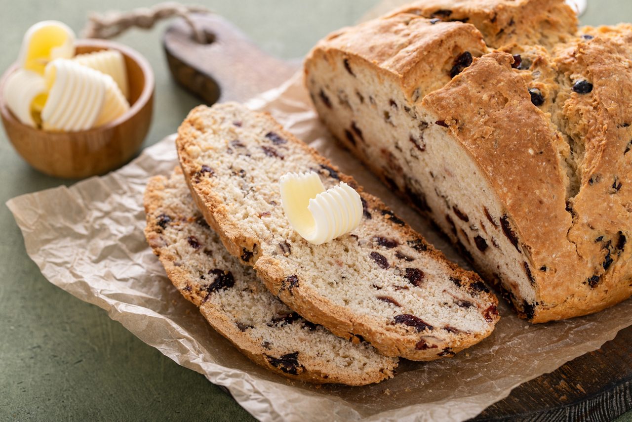 Soda bread in a cast iron pan with cranberries and pecans sliced and served with irish butter, irish recipe idea with St Patricks day