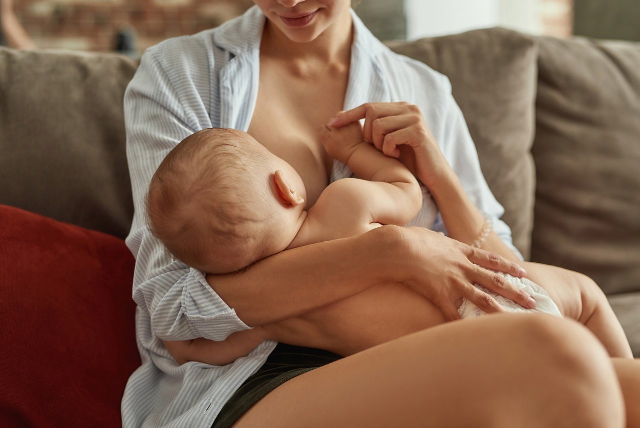Moeder die haar baby thuis borstvoeding geeft, wat borstvoeding, voeding voor zuigelingen en hechting tussen moeder en kind illustreert.