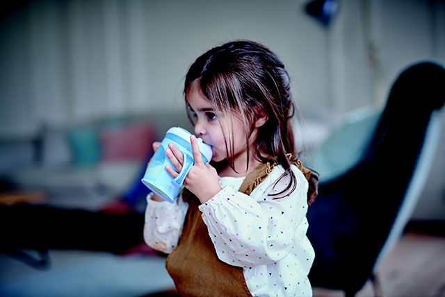 girl drinking from feeding beaker