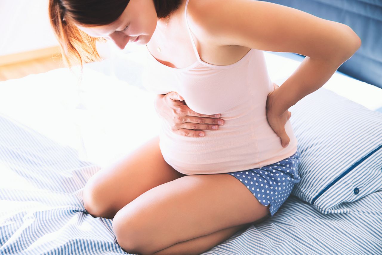 Pregnant woman suffering lower back pain. Woman getting a contraction and backache at home in the living room. Concept of pregnancy, maternity, health care, gynecology, medicine.