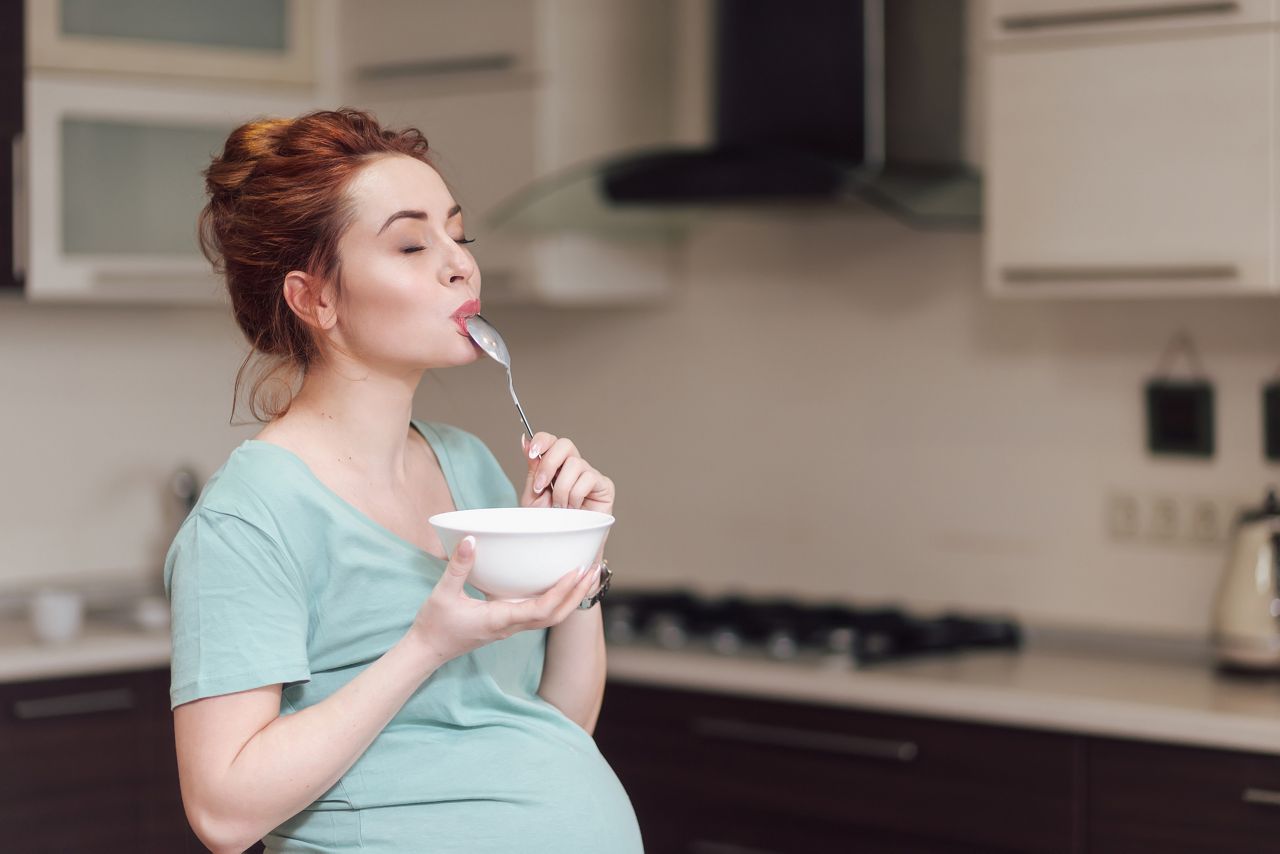 Beautiful pregnant woman eating with lust cereals on breakfast, enjoying meal. Yummy food for pregnant ladies