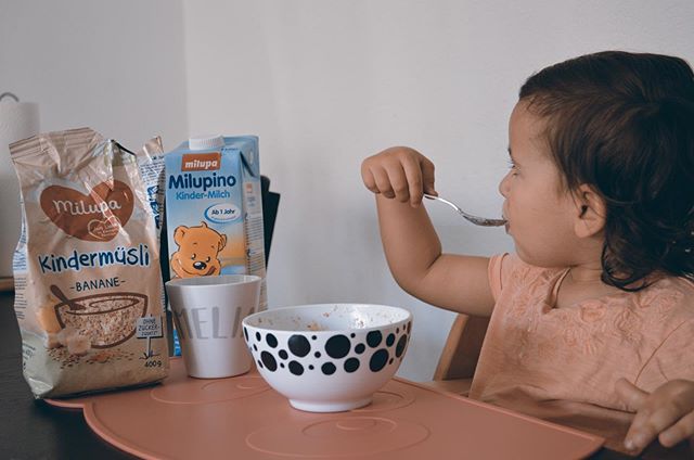 Kleinkind isst Brei mit Kindermüsli und Milupino im Hintergrund
