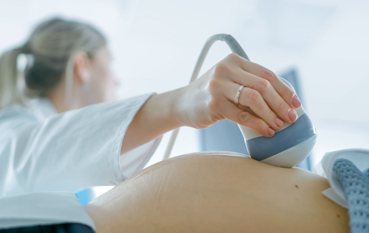 Une femme enceinte subissant une echographie realisee par un professionnel de la sante en milieu clinique. L image se concentre sur l appareil a ultrasons et l abdomen de la femme, mettant en evidence la procedure medicale. Le cadre est lumineux et professionnel, mettant l accent sur le soin et la precision.