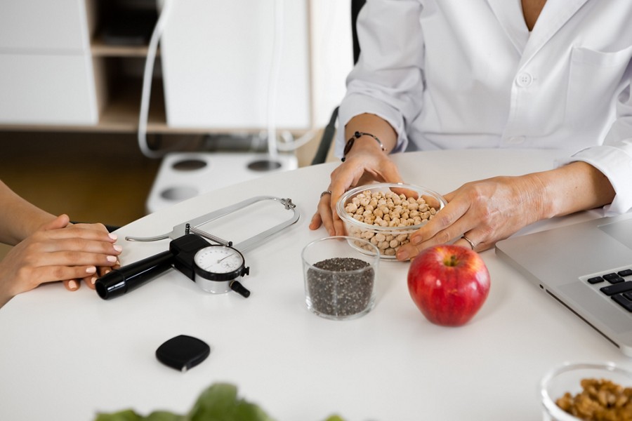 Hands of Crop dietitian with bowl of chickpeas, sitting at desk with laptop and nutrient ingredients.