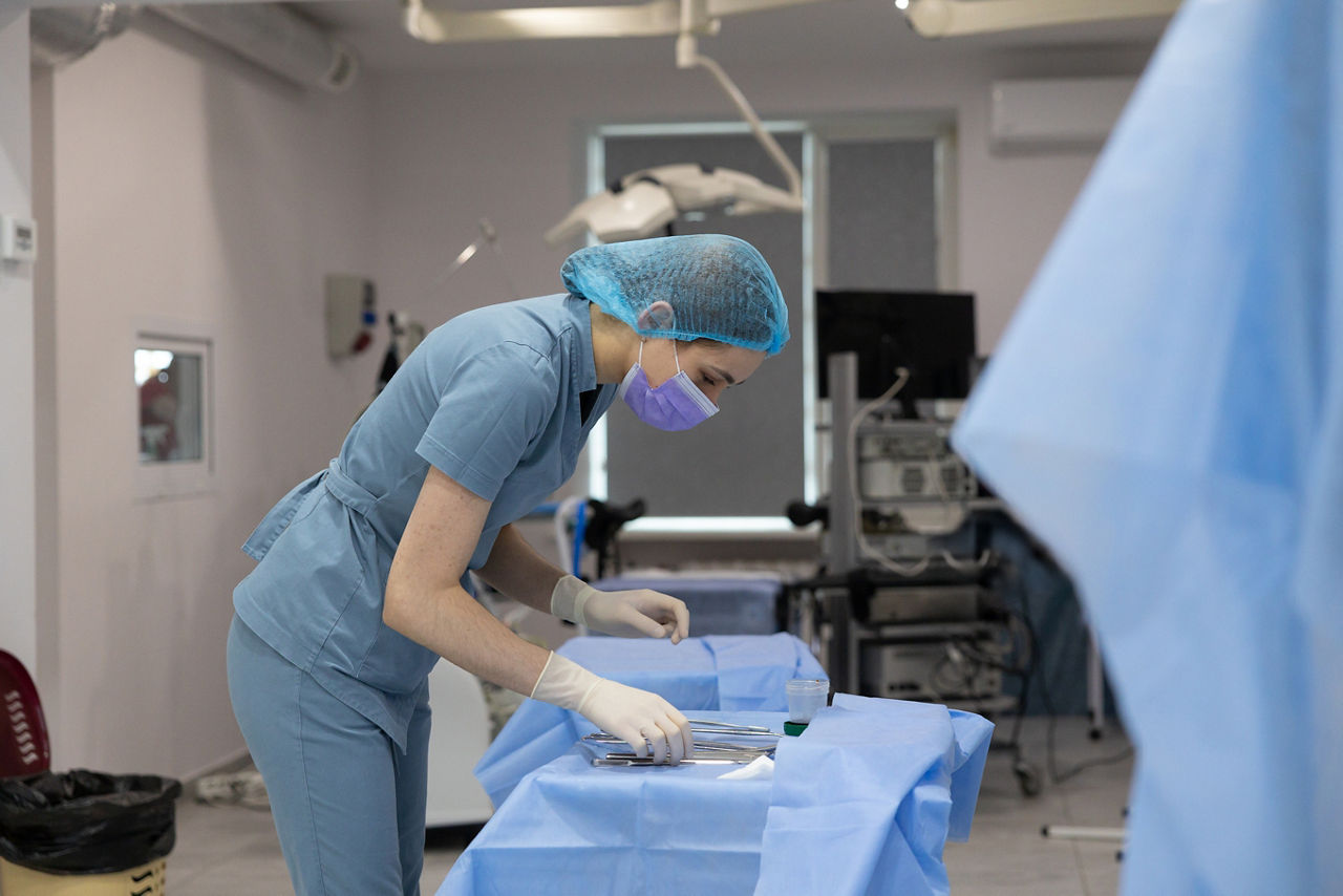 The operating nurse lays out sterile surgical instruments on the table. The table is covered with the surgical drape.