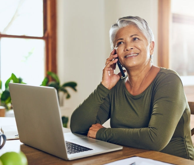 A woman sitting in front of a laptop and using her phone