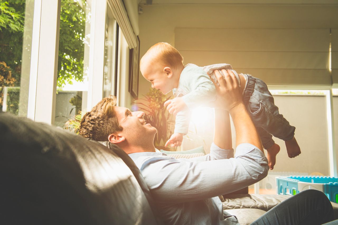 Caucasian father sitting on sofa lifting baby son