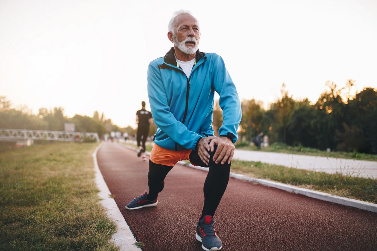 Senior bearded man jogging on a running track outdoors, in a tracksuit.