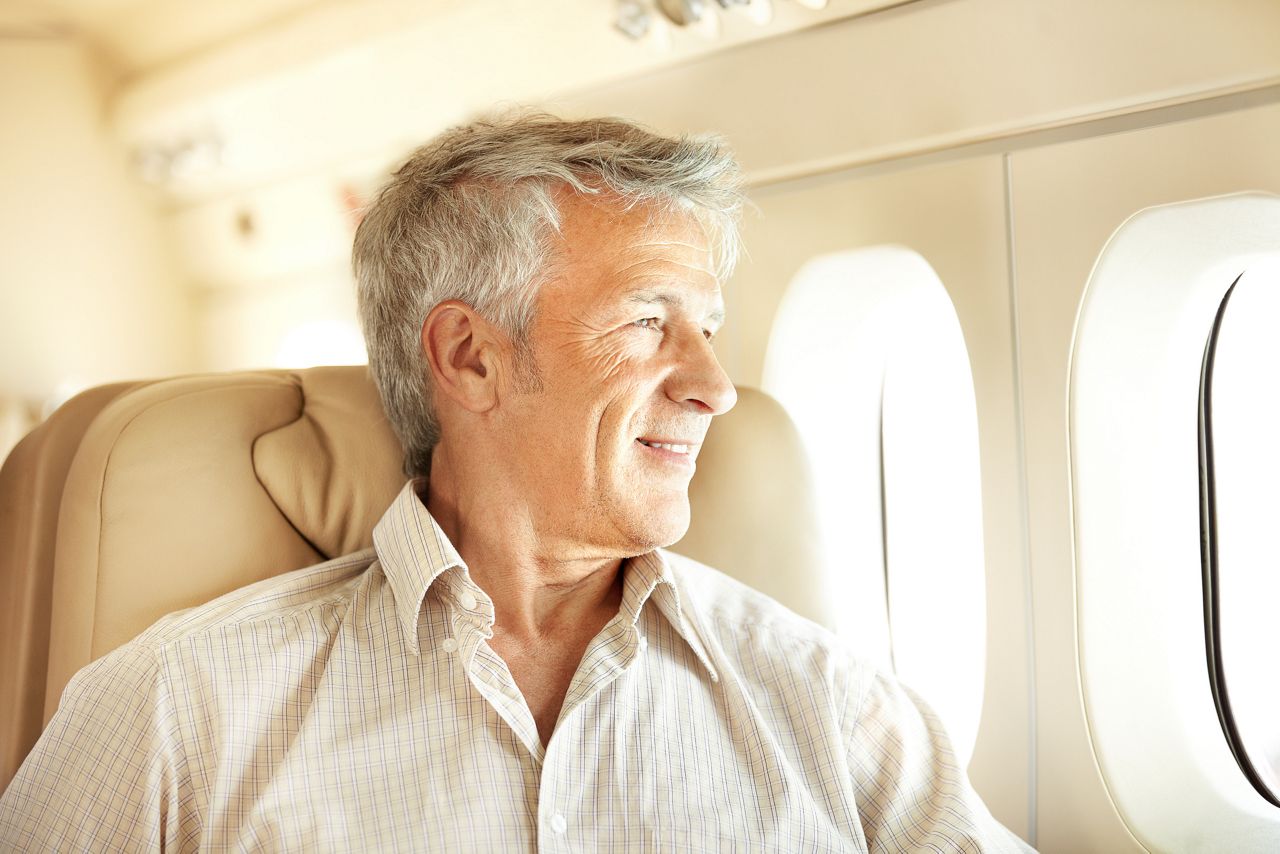Handsome senior man sitting in an airplane with a smile and looking out the window
