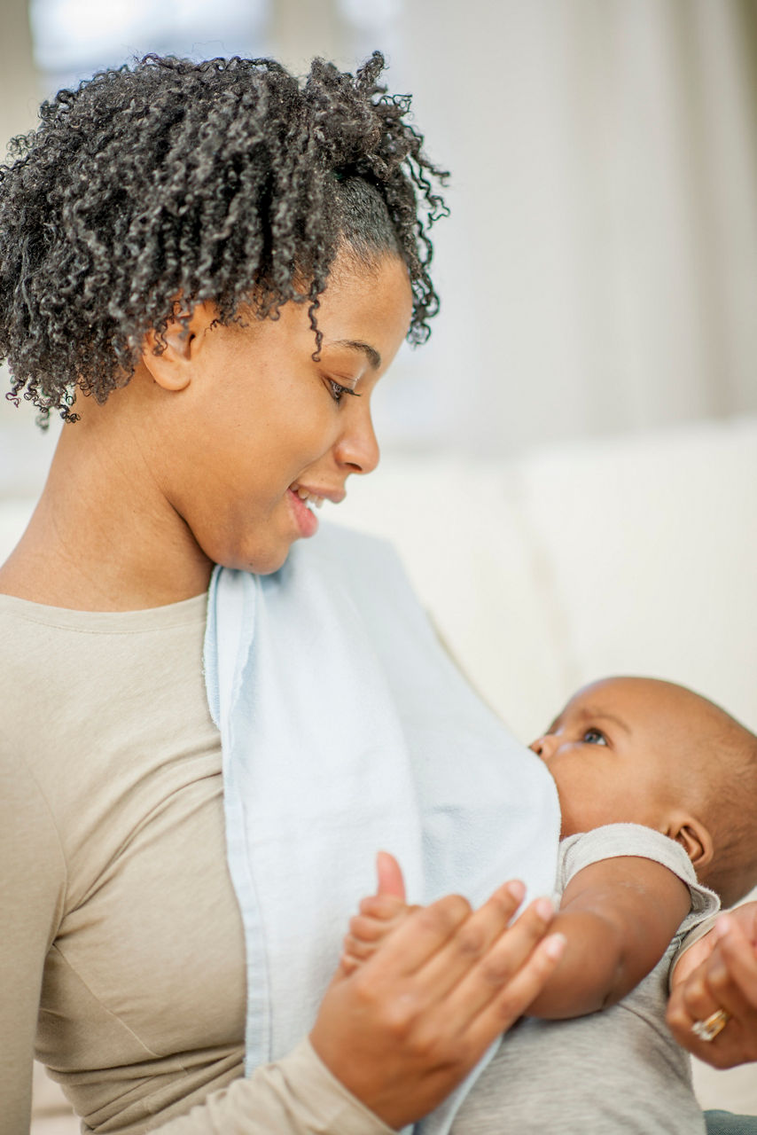 A mother is breastfeeding her little boy happily in their home.