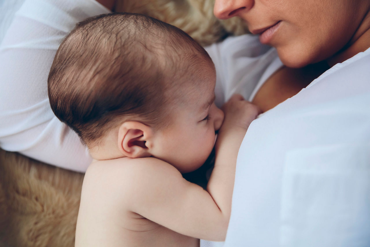 Top view of newborn baby girl lying on the bed embraced by her mother